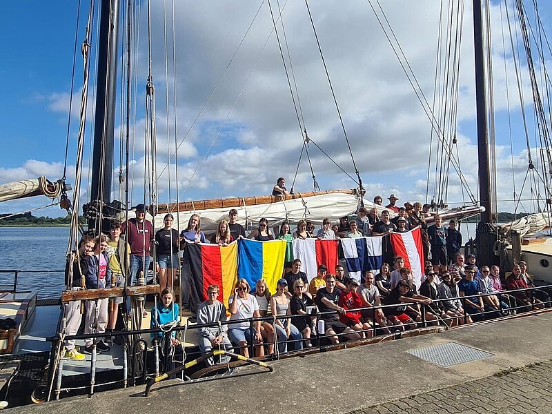Gruppenfoto, ca. 60 Jugendliche stehen mit den Flaggen von Österreich, Finnland, Polen, Ukraine und Deutschland an Bord eines Segelschiffes.