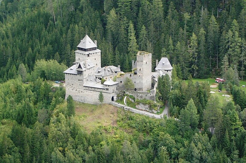 Eine Burg, die in einer bewaldeten Gebirgslandschaft steht.
