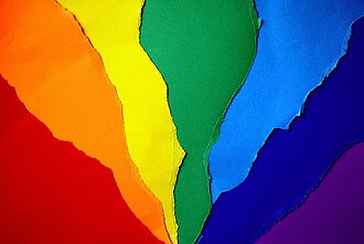 Das Bild zeigt aufeinanderliegende Papiere in Regenbogenfarben.