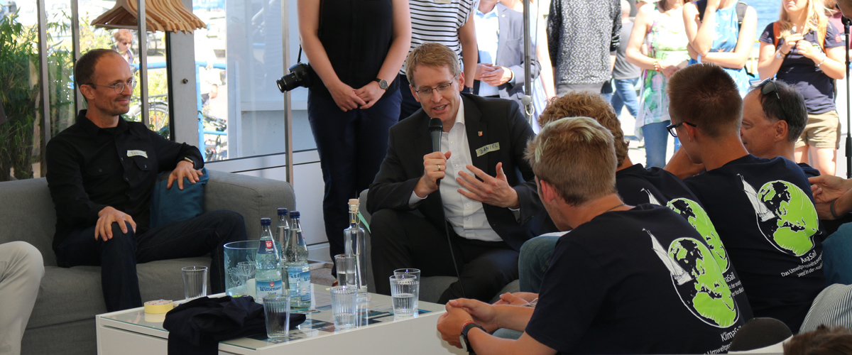 Ministerpräsident Daniel Günther im Gespräch mit Jugendlichen. Diese tragen T-Shirts mit dem Logo von KlimaSail.