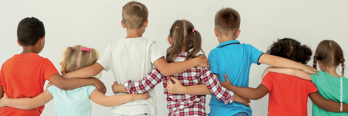 7 Kinder, verschiedener Hautfarbe, in bunter Kleidung, stehen vor einem grauen Hintergrund. Zusehen sind sie von hinten. Sie stehen nebeneinander und haben einander die Arme auf die Schultern gelegt.